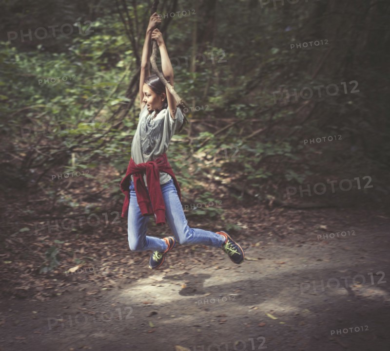 Mixed race girl swinging from tree branch on dirt path