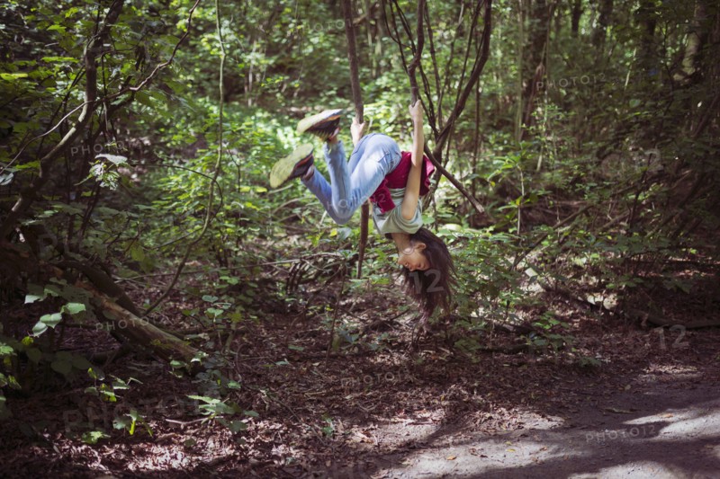 Mixed race girl swinging from tree branch on dirt path