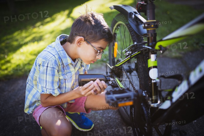 Mixed race boy oiling bicycle chain in backyard