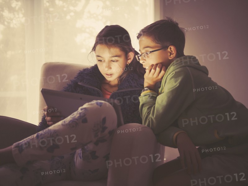 Mixed race children using digital tablet in living room
