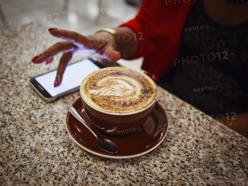 Mixed race woman using cell phone with coffee in cafe