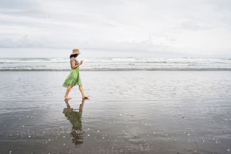Mixed race woman walking on beach with cell phone