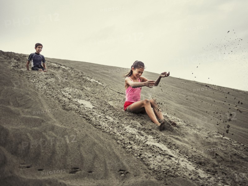 Children sliding on sand dune