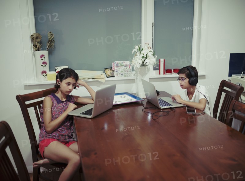 Mixed Race brother and sister using laptops at table