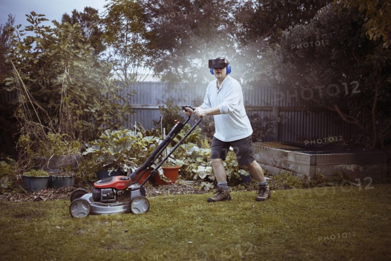 Caucasian man mowing lawn with VR goggles