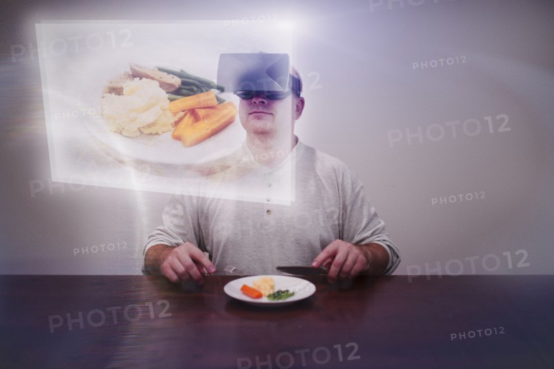 Caucasian man imagining larger meal with VR goggles