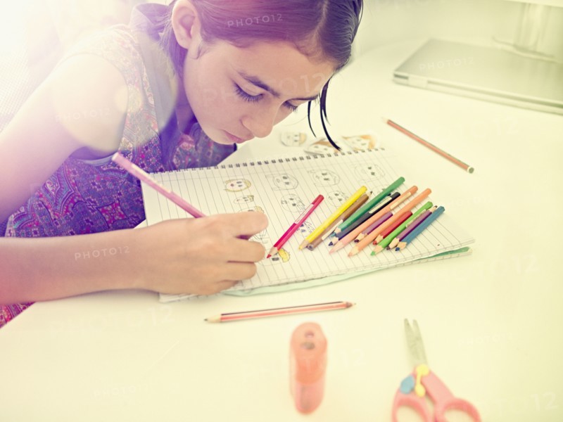 Mixed Race girl drawing faces in notebook