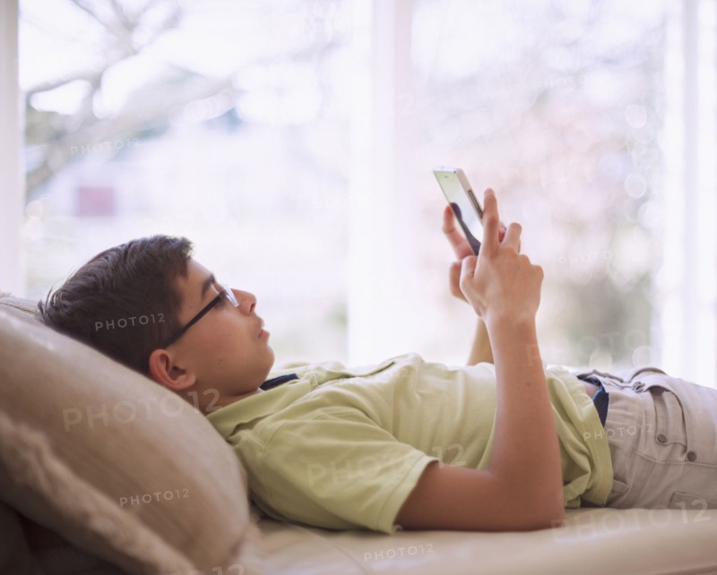 Mixed Race boy texting on cell phone near window
