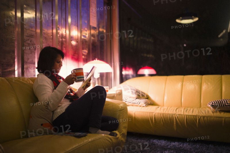 Woman drinking tea and reading magazine on sofa