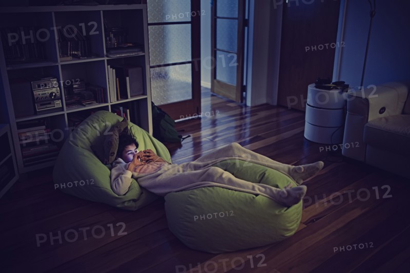 Mixed Race girl using cell phone laying on bean bags in dark