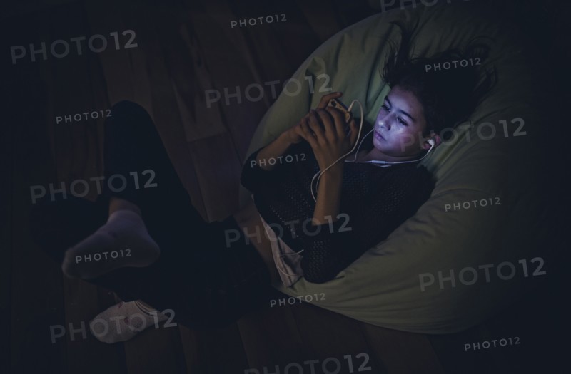 Mixed Race girl using cell phone laying on bean bag in dark