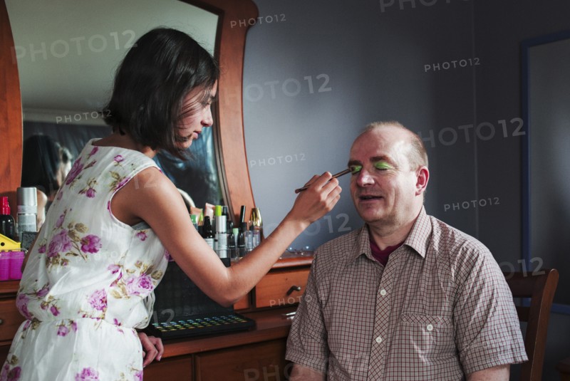 Girl applying makeup to eyes of father