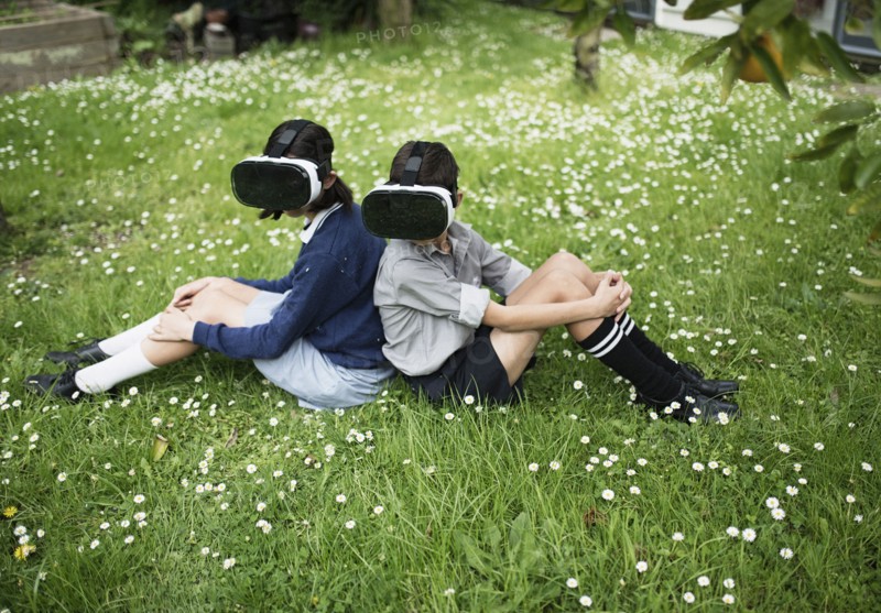 Mixed Race brother and sister sitting in grass wearing virtual reality goggles