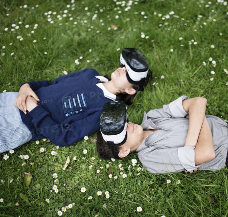 Mixed Race brother and sister laying in grass wearing virtual reality goggles