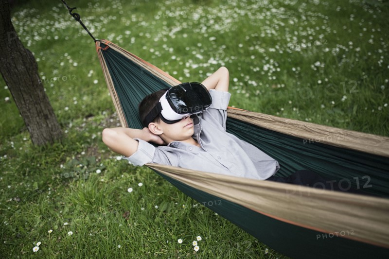 Mixed Race boy laying in hammock wearing virtual reality goggles