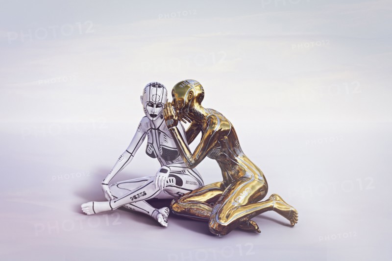 Gold female cyborg sitting and whispering to white cyborg