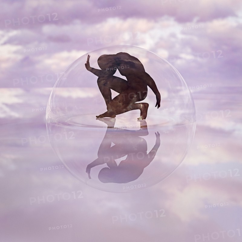 Naked man crouching in transparent sphere