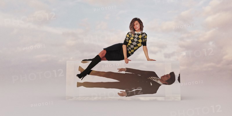 Confident businesswoman sitting on cube with businessman trapped inside