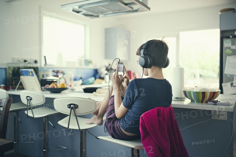 Mixed race boy sitting in kitchen listening to cell phone
