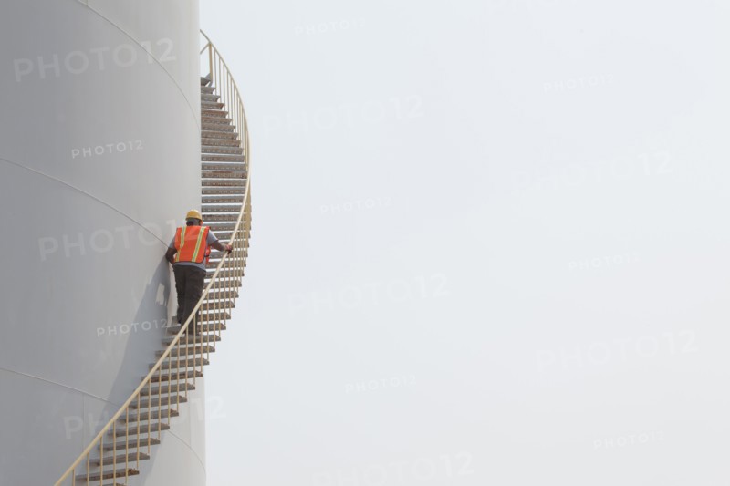 Mixed race worker climbing staircase on storage tank
