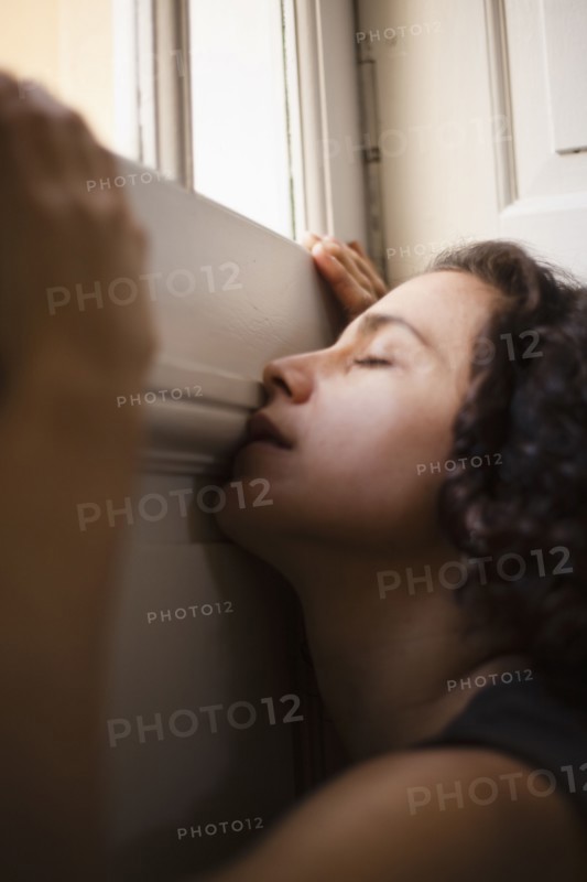 Mixed race woman leaning on wall near window
