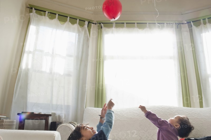 Mixed race children playing with balloon in living room