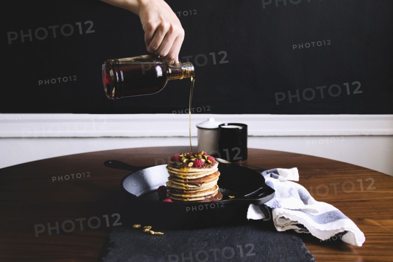 Hand pouring syrup on pancakes