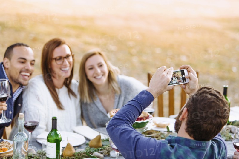 Man photographing friends at outdoor table
