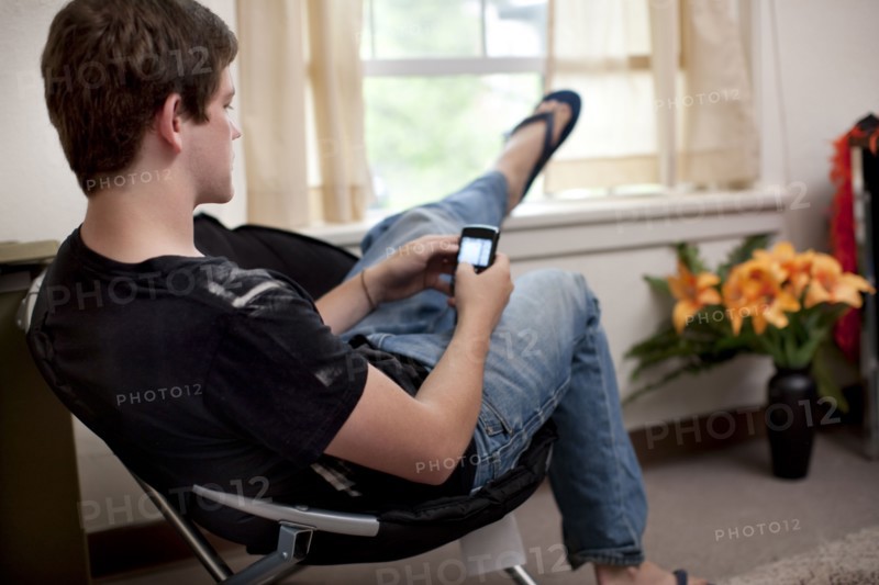 Caucasian man text messaging on cell phone in dorm room