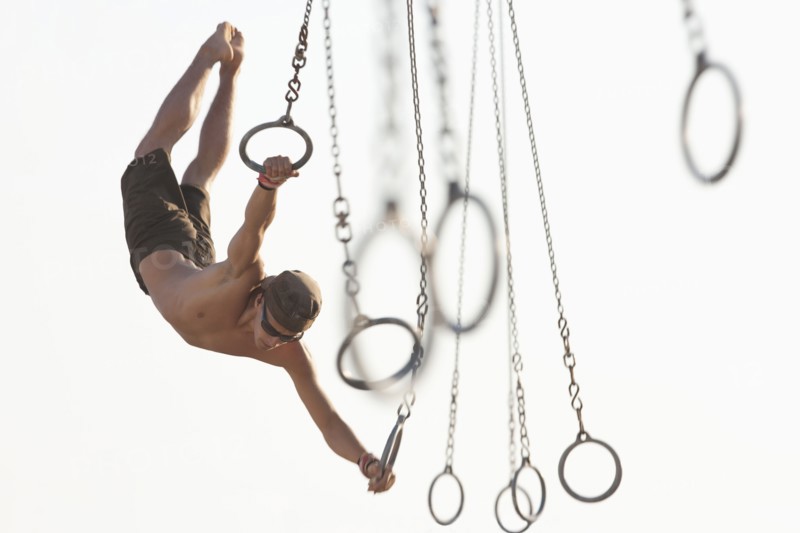 Mixed race man swinging on athletic rings