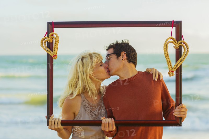 Caucasian couple holding frame with hearts and kissing