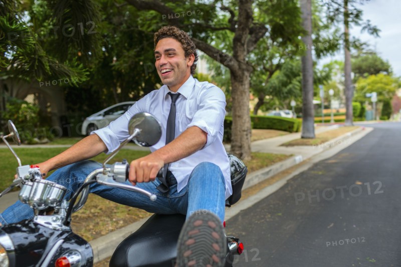 Hispanic businessman driving moped on neighborhood road