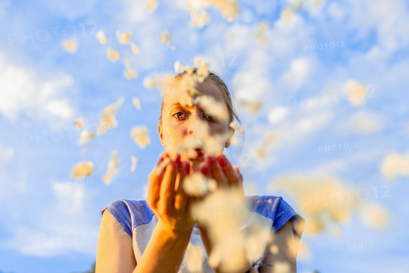 Caucasian teenage girl blowing flower petals under blue sky