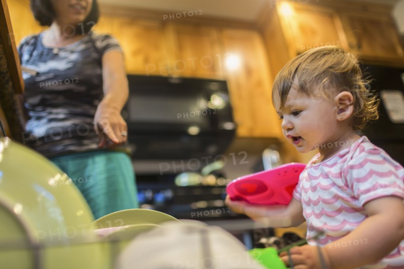 Baby girl helping mother load dishwasher