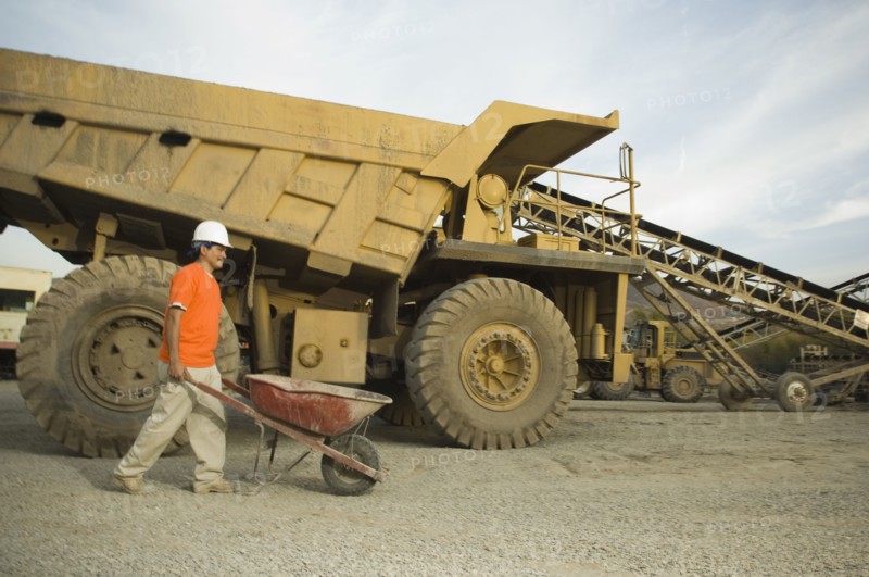 Hispanic man pushing wheelbarrow at gravel plant
