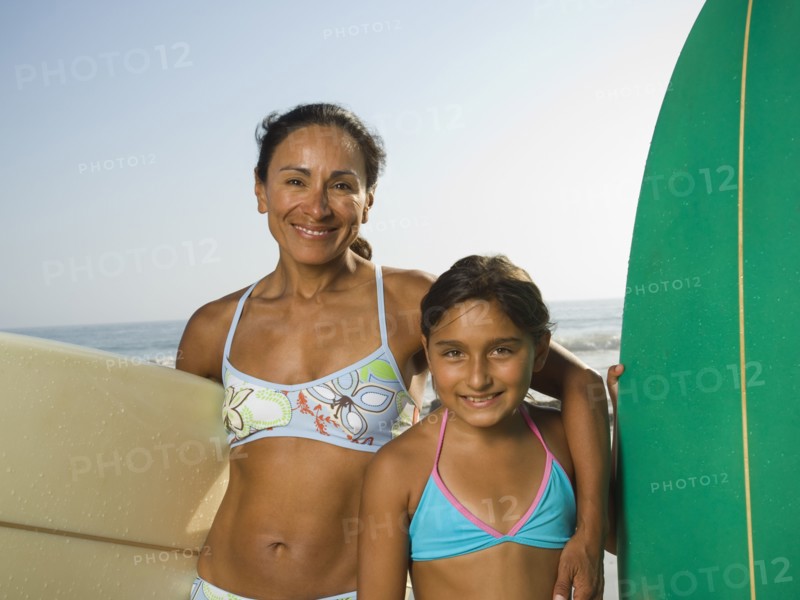 Hispanic mother and daughter holding surfboards