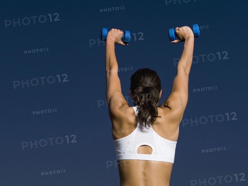 Rear view of mixed race woman holding dumbbells overhead