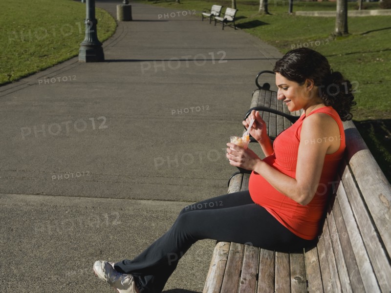 Pregnant Middle Eastern woman eating fruit in park
