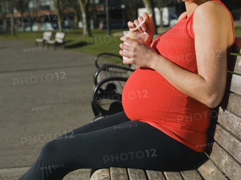 Pregnant Middle Eastern woman eating fruit in park