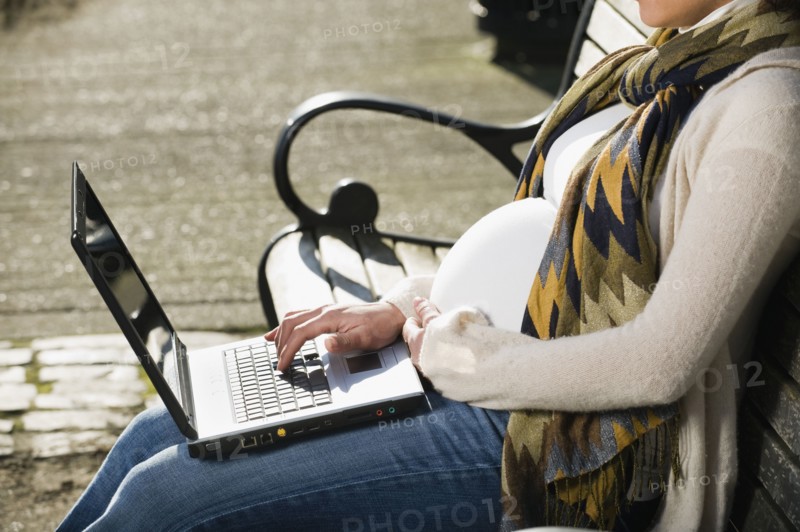 Pregnant Middle Eastern woman using laptop on park bench