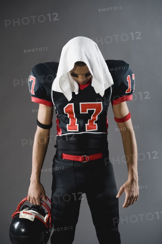 Mixed race football player looking down with towel on head
