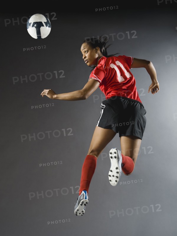Mixed race soccer player in air with soccer ball
