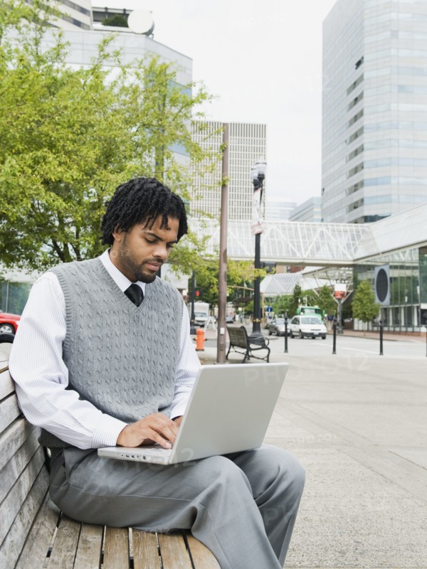 Mixed race businessman using laptop on city bench