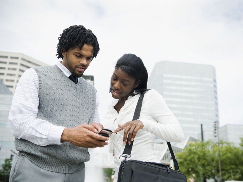 Businessman and businesswoman looking at cell phone in city