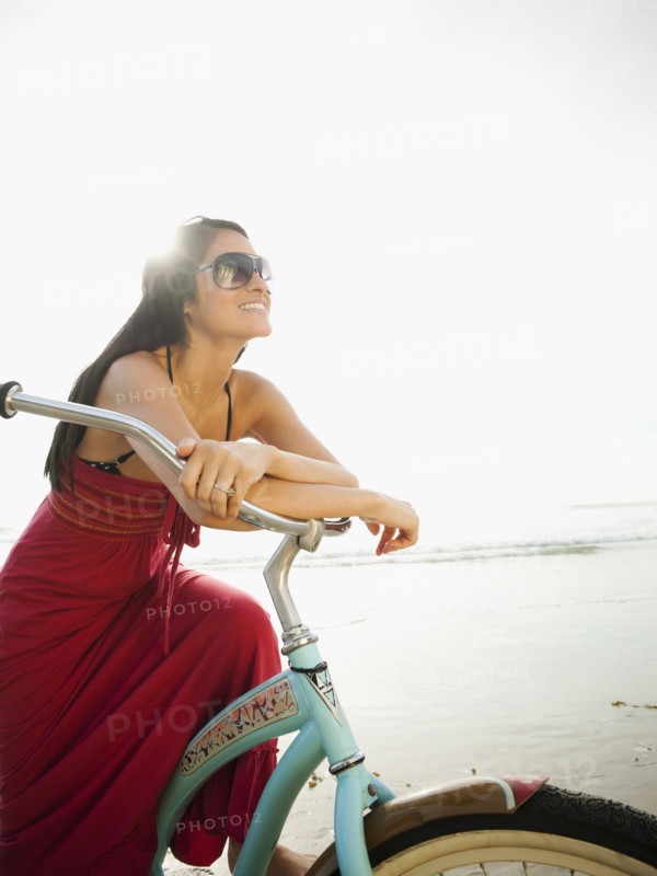 Hispanic woman riding retro bicycle on beach
