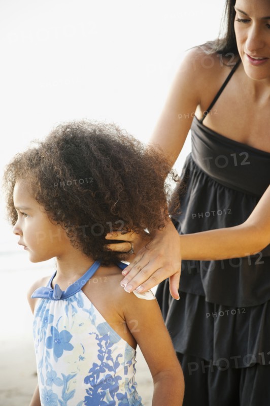 Hispanic mother rubbing sunscreen on daughter at beach