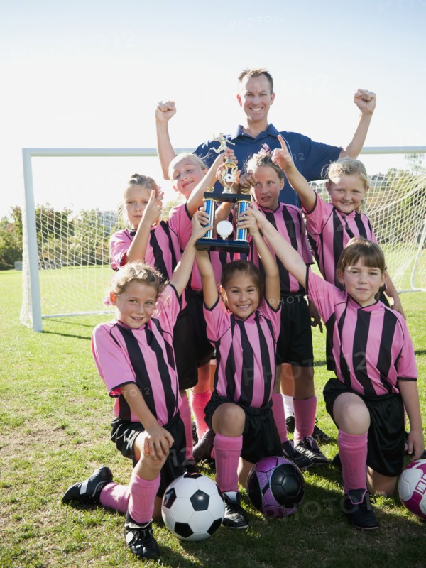 Coach and girl soccer players posing with trophy