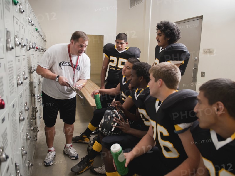 Coach talking to football players in locker room