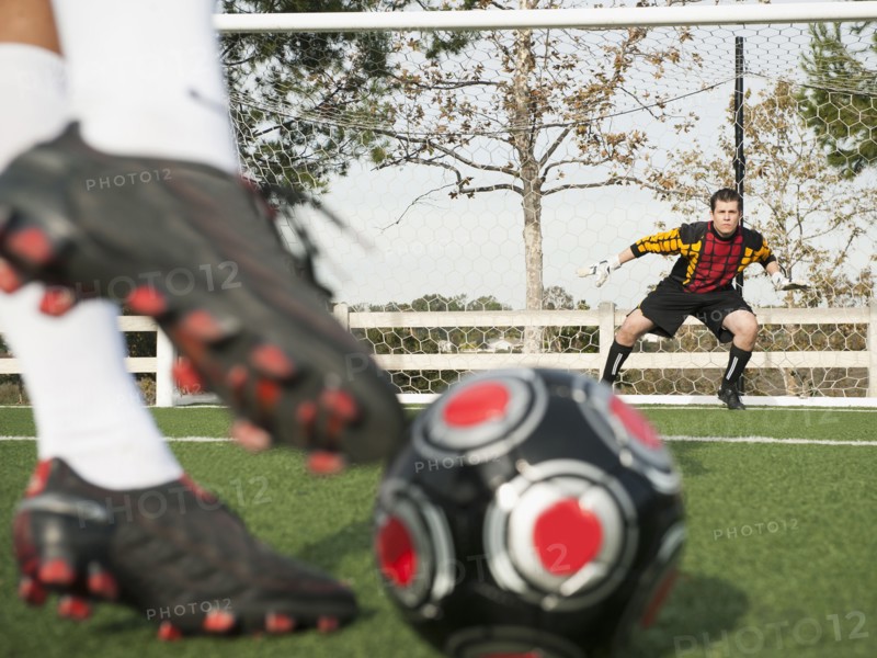 Soccer player kicking ball into goal on soccer field