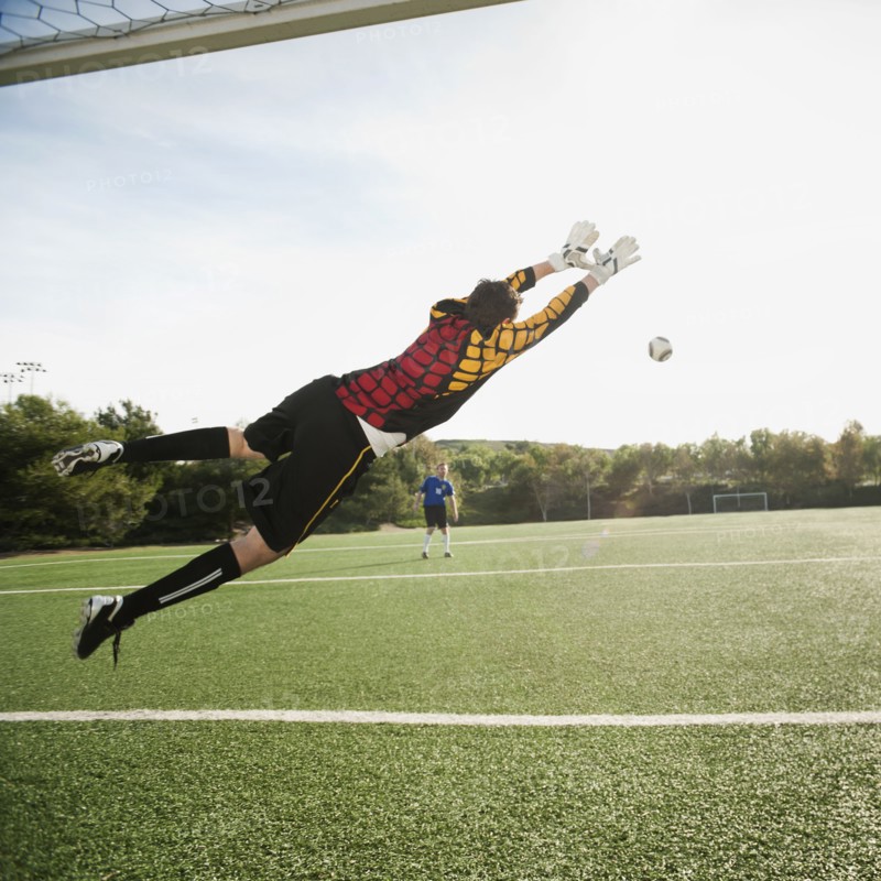 Mixed race goalkeeper in mid-air protecting goal